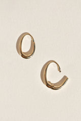 A pair of polished oval-shaped gold hoop earrings, displayed on a textured off-white background, one with a hinge open.