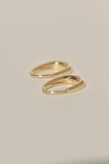 A pair of thin gold huggie hoop earrings on a plain, warm off-white background.