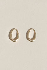 A pair of gold-toned, open hoop earrings with a satin finish, displayed on a light beige textured background.