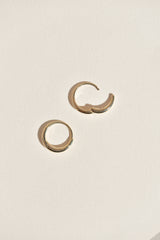 A pair of gold hinged hoop earrings on a textured off-white background with one hoop open.