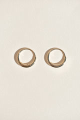 A pair of thin gold hoop earrings with a polished finish, displayed side-by-side on a textured off-white background.