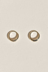 A pair of small gold huggie hoop earrings on a textured off-white background.