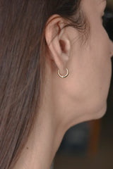 A close-up side profile of a woman wearing a small gold huggie hoop earring.
