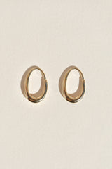 A pair of polished gold-toned oval hoop earrings displayed on a textured off-white background.