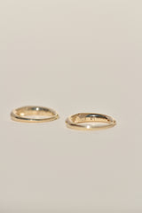 Two thin gold hoops displayed side by side on a plain, warm off-white background.