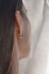 A close-up side profile of a woman wearing a small gold hoop earring, with her hair and ear clearly visible against a soft light background.