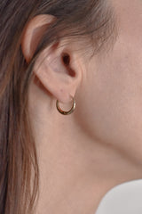 A close-up of a person's ear wearing a small, thin gold hoop earring.