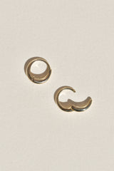 A pair of hinged gold hoop earrings on a textured off-white background, with one earring open.