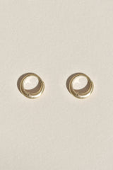 A pair of small gold huggie hoop earrings in a satin finish on a textured off-white background.
