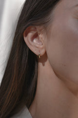 A close-up of a model's ear wearing a delicate gold huggie hoop earring.